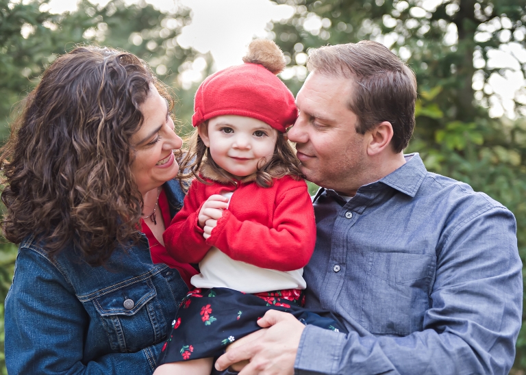 Mother and father holding toddler girl and looking at her at christmas tree farm in North Attleboro, MA